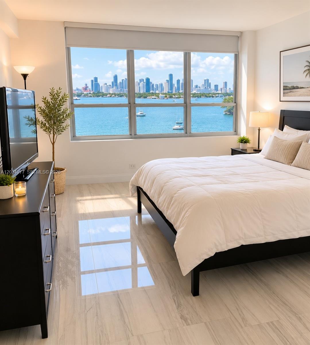 A bedroom features a bed, a black dresser, and a large window overlooking a city skyline — MIAMI BEACH, FL
