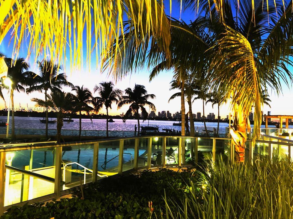 A view of a waterfront pool area at dusk with palm trees and city skyline — MIAMI BEACH, FL