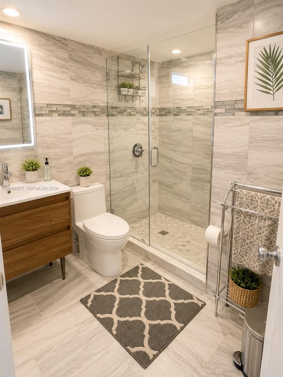 A modern bathroom features a glass-enclosed shower, a wood vanity, and light-colored tile walls — MIAMI BEACH, FL