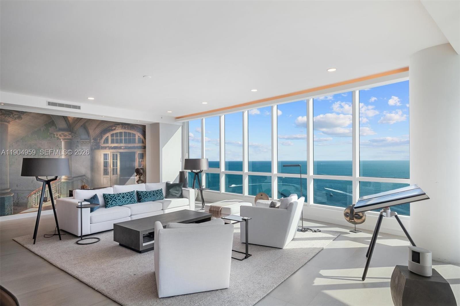 A modern living room features floor-to-ceiling windows with ocean views and a large wall mural — 100 S Pointe Dr # 3203, Miami Beach FL 33139, MIAMI BEACH, FL