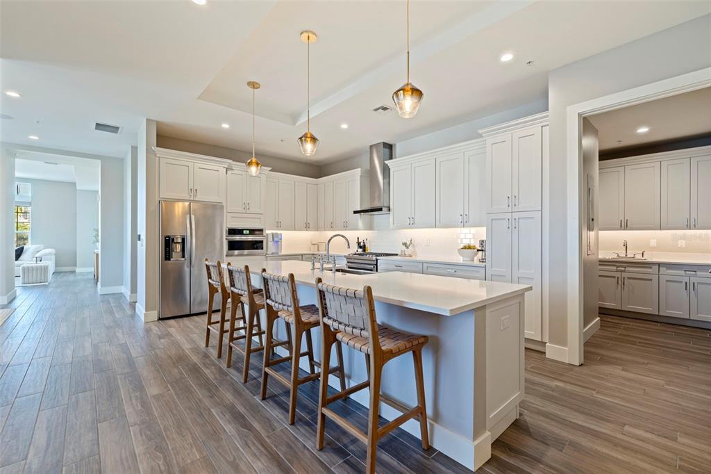 A modern kitchen features white cabinetry, a large island with bar stools, and wood flooring — 91 DAVIS BOULEVARD UNIT 201, TAMPA, FL