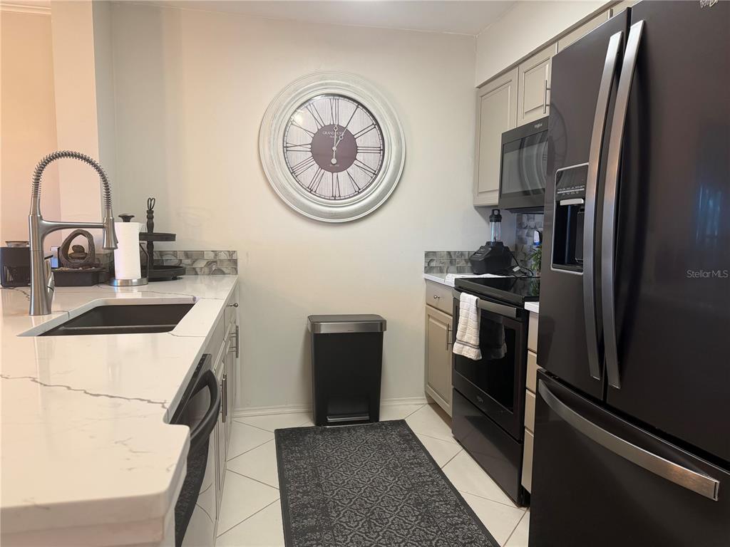 A kitchen features white countertops, light-colored cabinets, a black refrigerator, and a large wall clock — 2400 FEATHER SOUND DRIVE UNIT 213, CLEARWATER, FL