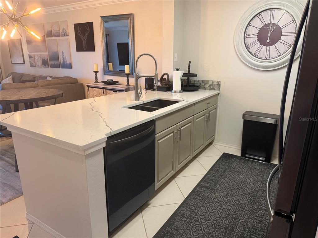 A kitchen island features a sink, dishwasher, and white countertops with gray cabinets — 2400 FEATHER SOUND DRIVE UNIT 213, CLEARWATER, FL
