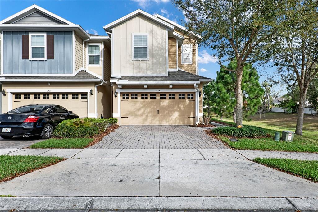 The exterior of a two-story townhome features a beige garage, brick driveway, and blue siding — 1335 E 10TH STREET, APOPKA, FL