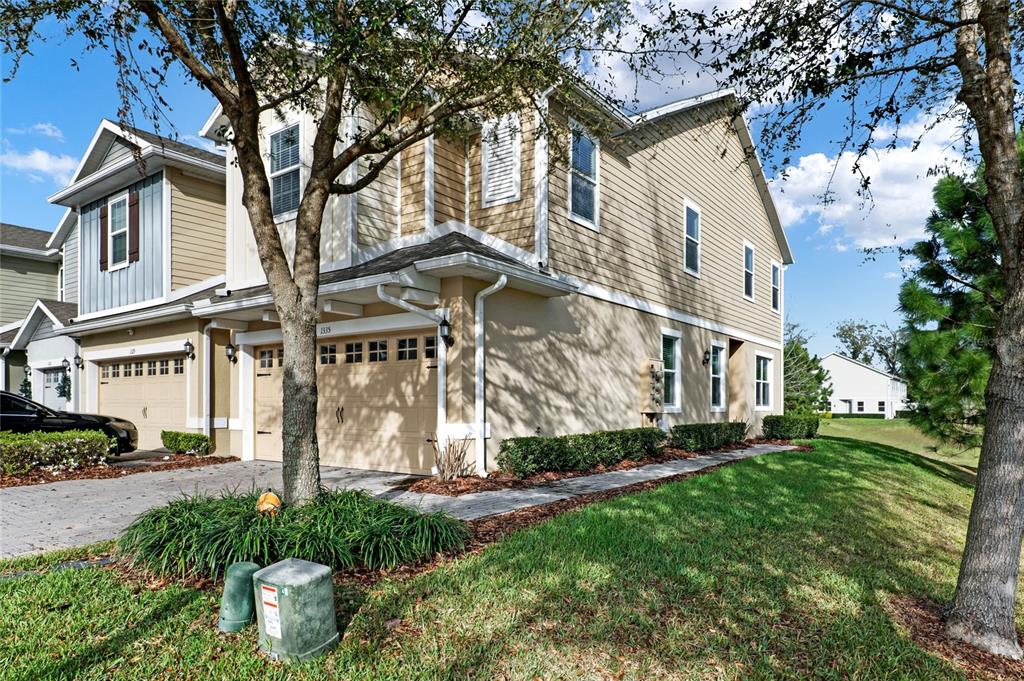 A two-story townhouse with tan siding, a two-car garage, and a paved driveway — 1335 E 10TH STREET, APOPKA, FL
