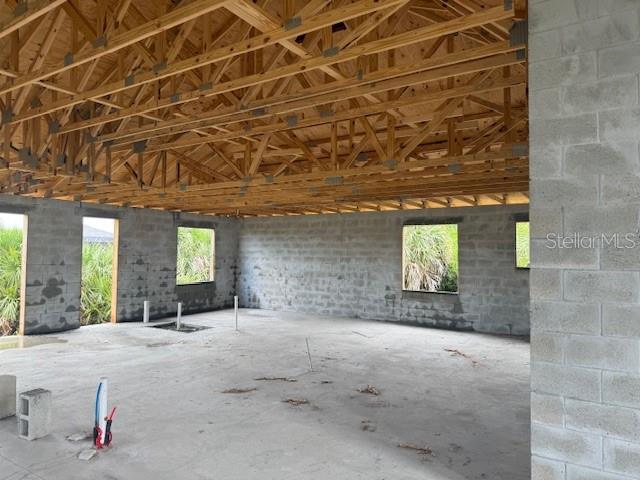 An unfinished room with concrete block walls, a wooden truss ceiling, and exposed plumbing pipes — 10510 RAINSVILLE STREET, PORT CHARLOTTE, FL