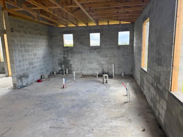 An unfinished room with concrete block walls, exposed wood ceiling joists, and exposed plumbing pipes — 10510 RAINSVILLE STREET, PORT CHARLOTTE, FL
