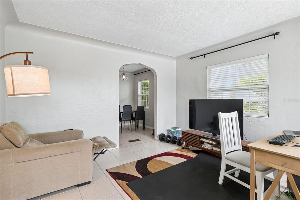 A living room with a recliner, television, desk, and an arched doorway leading to a dining area — 1500 30TH AVENUE N, ST PETERSBURG, FL