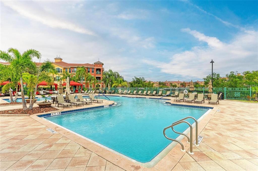 A swimming pool with lounge chairs and palm trees sits in front of apartment buildings — 2738 VIA TIVOLI UNIT 231B, CLEARWATER, FL