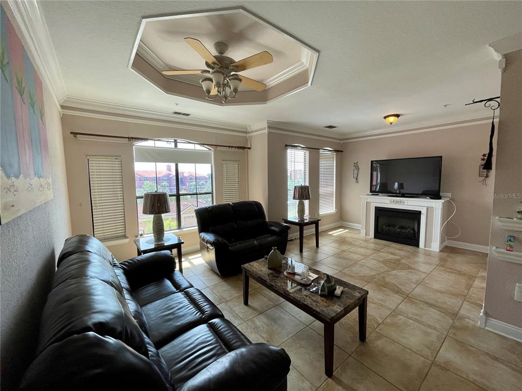 A living room features tile flooring, a tray ceiling with a fan, and a fireplace — 2738 VIA TIVOLI UNIT 231B, CLEARWATER, FL