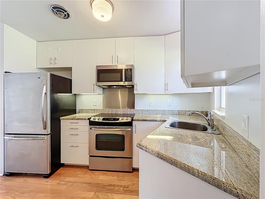 A kitchen features white cabinets, stainless steel appliances, and granite countertops over wood flooring — 640 N PARK AVENUE UNIT 4, WINTER PARK, FL