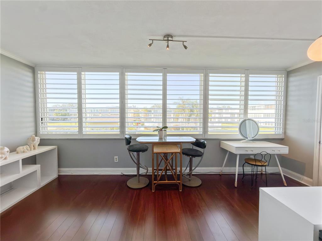 A room with dark wood floors, white plantation shutters, a small table, and a desk — 8100 DR MARTIN LUTHER KING JR STREET N UNIT 202, ST PETERSBURG, FL