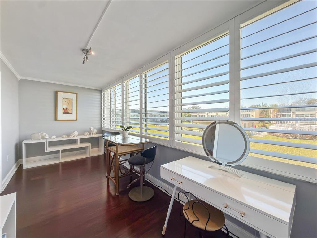 A sunroom features dark wood flooring, white plantation shutters, a vanity, and a small dining table — 8100 DR MARTIN LUTHER KING JR STREET N UNIT 202, ST PETERSBURG, FL