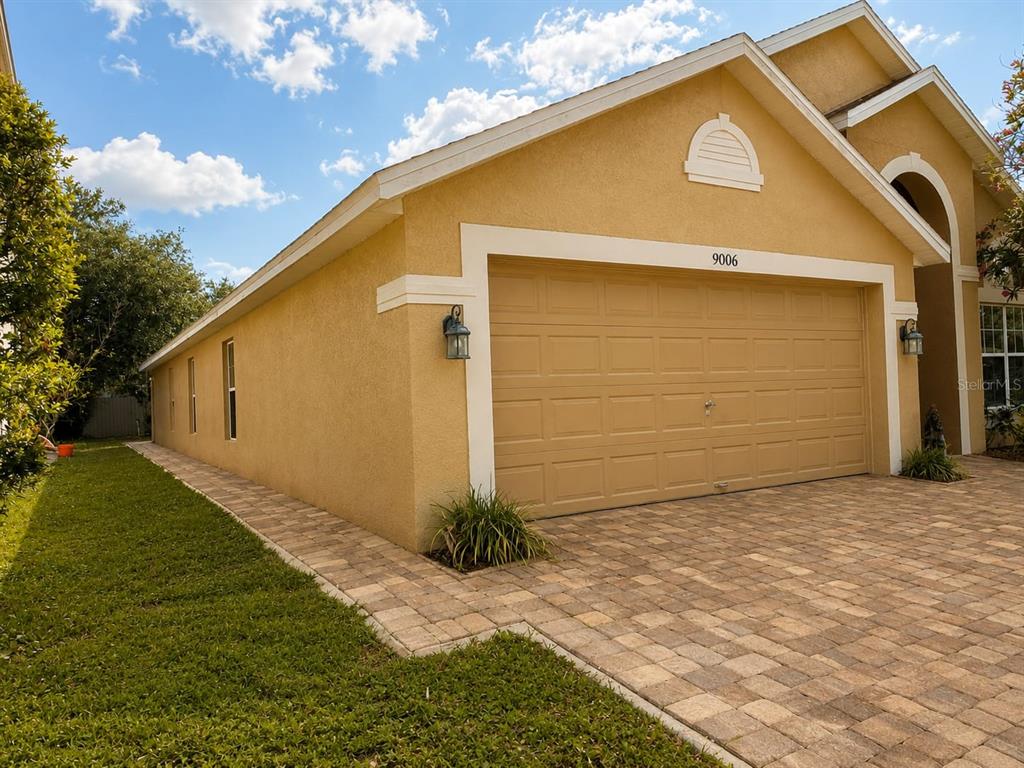 A tan house exterior features a two-car garage, a paved driveway, and a side lawn — 9006 VERONA SOUND WAY, ORLANDO, FL