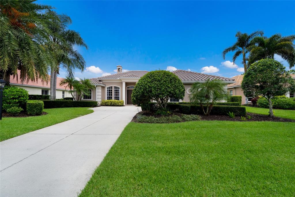 A single-story house with a concrete driveway, manicured landscaping, and palm trees under a blue sky — 7058 TWIN HILLS TERRACE, LAKEWOOD RANCH, FL