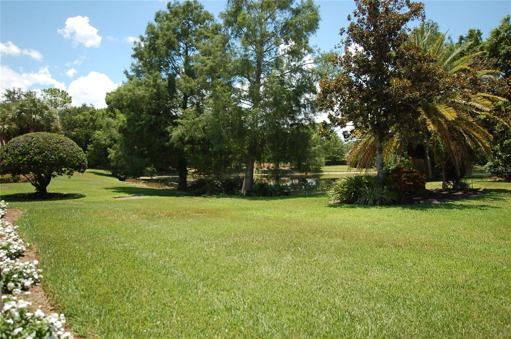 A grassy lawn leads to a small pond surrounded by mature trees and landscaping — 7058 TWIN HILLS TERRACE, LAKEWOOD RANCH, FL
