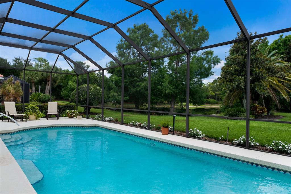 A screened-in swimming pool overlooks a grassy backyard with trees and a pond — 7058 TWIN HILLS TERRACE, LAKEWOOD RANCH, FL
