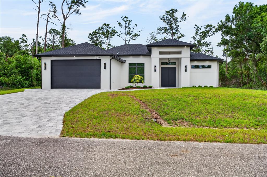 A modern, single-story house with a white stucco exterior, dark roof, and a paved driveway — 3491 KACHER ROAD, NORTH PORT, FL