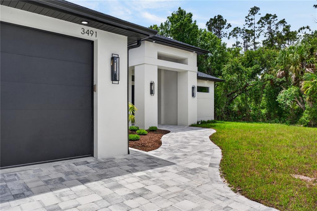 A modern house exterior features a gray garage door, white walls, and a paver walkway — 3491 KACHER ROAD, NORTH PORT, FL