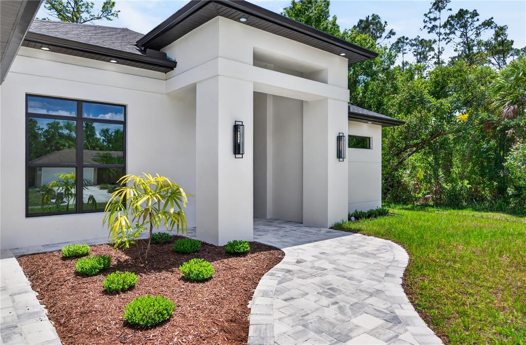 A modern white house exterior features a stone walkway, a small tree, and landscaping — 3491 KACHER ROAD, NORTH PORT, FL