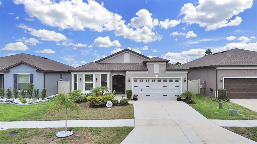 A single-story suburban house with a gray stucco exterior, a two-car garage, and a driveway — 11121 GREEN HARVEST DRIVE, RIVERVIEW, FL
