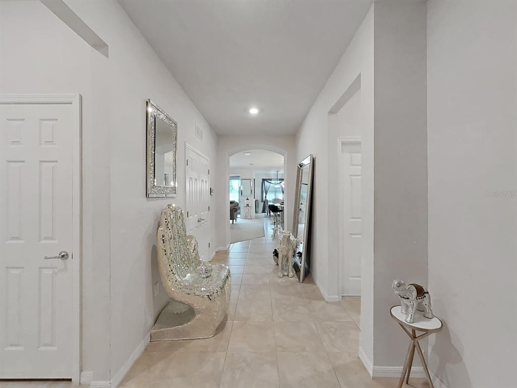 A bright hallway features tiled floors, white doors, a mirrored chair, and a floor mirror — 11121 GREEN HARVEST DRIVE, RIVERVIEW, FL