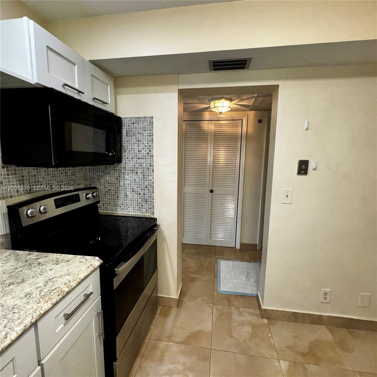 A kitchen features white cabinets, a black stove, a microwave, and a tiled backsplash — 215 SE 3rd Ave # 203A, Hallandale Beach FL 33009, HALLANDALE BEACH, FL