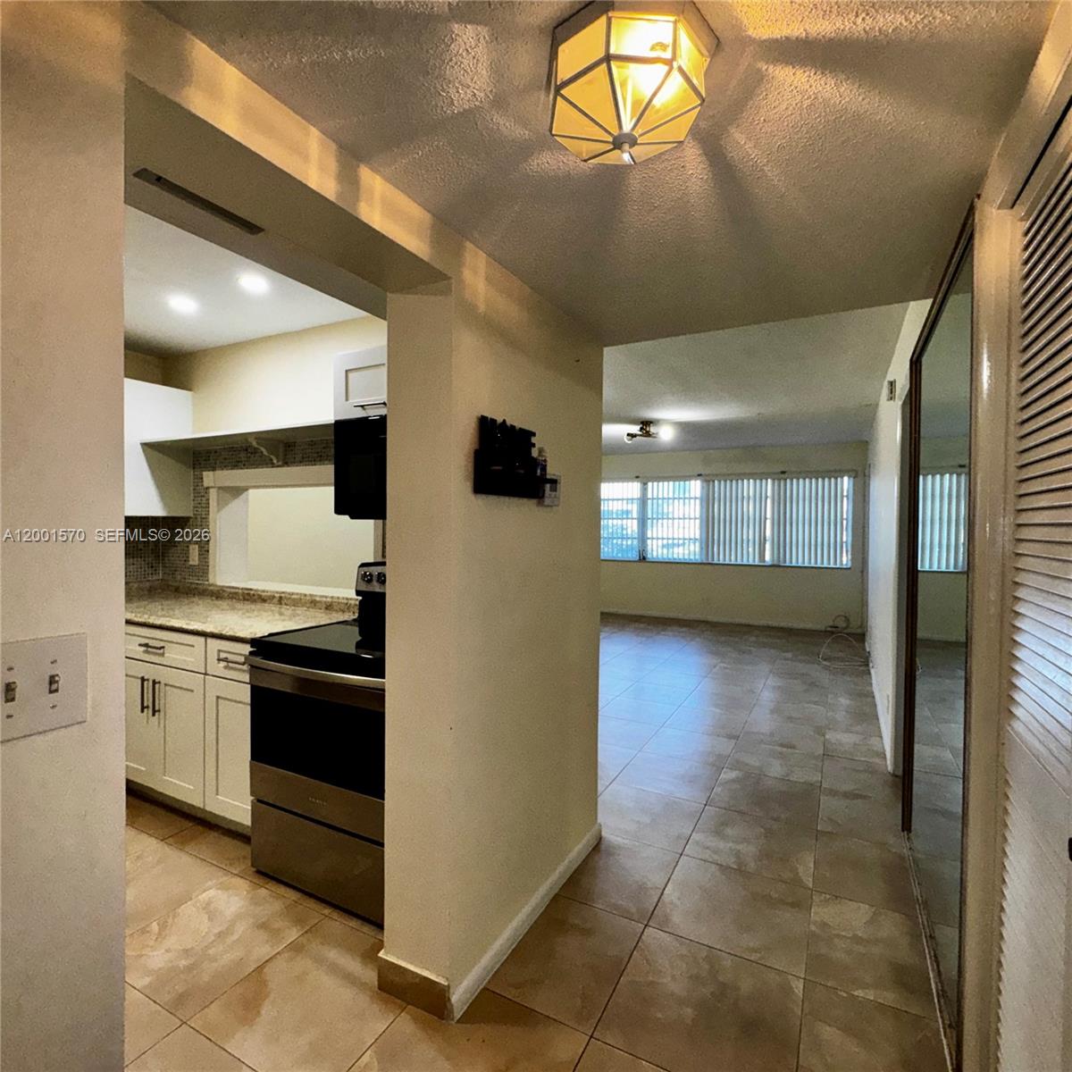 A kitchen with white cabinets and stainless steel appliances opens into a tiled living area — 215 SE 3rd Ave # 203A, Hallandale Beach FL 33009, HALLANDALE BEACH, FL