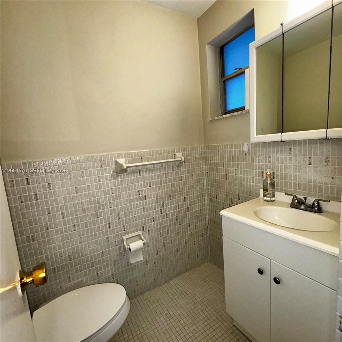 A small bathroom features a toilet, a vanity with a sink, and tiled walls — 215 SE 3rd Ave # 203A, Hallandale Beach FL 33009, HALLANDALE BEACH, FL