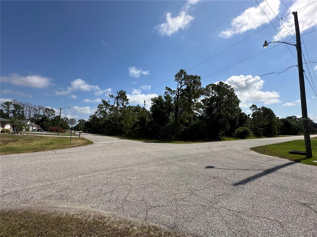 An asphalt road intersection features a utility pole and a wooded lot under a blue sky — 18038 YORK AVENUE, PORT CHARLOTTE, FL