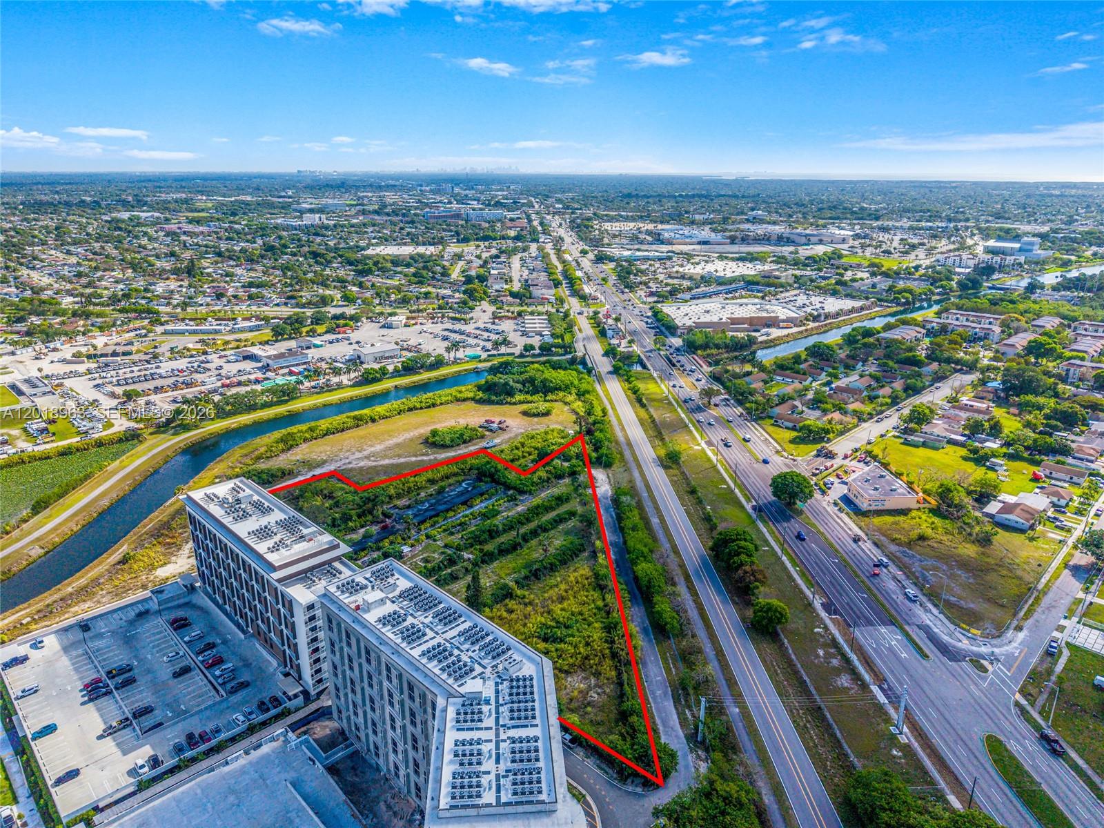 An aerial view shows a vacant, overgrown lot outlined in red next to a large building — 21281 SW 117th Ave, Miami FL 33177, MIAMI, FL