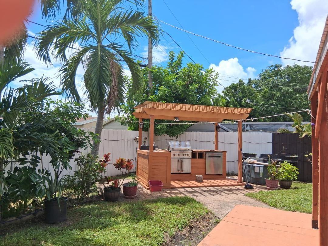 An outdoor kitchen with a wooden pergola, stainless steel grill, and appliances on a patio — 7040 SW 29th Street, Miramar FL 33023, MIRAMAR, FL