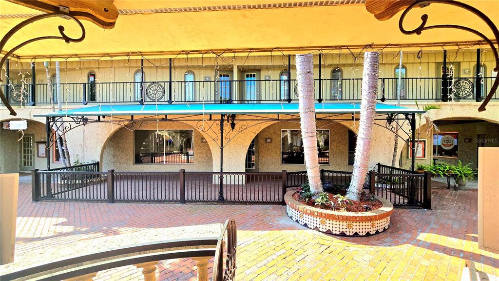 A brick courtyard features a covered patio, a central planter with two trees, and balconies — 530 US-41-BYP UNIT 20-21A, VENICE, FL