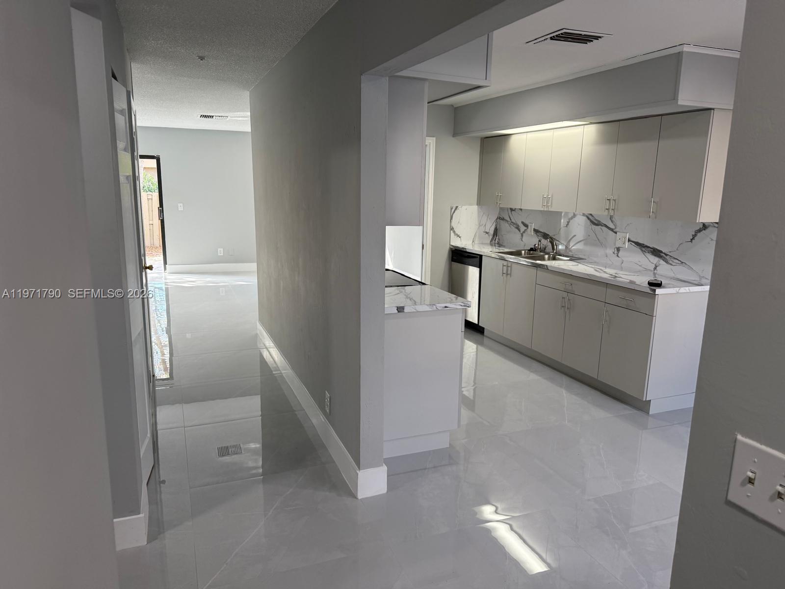 A kitchen with gray cabinets and marble-patterned countertops opens to a hallway with tile flooring — 2700 N 34th Ave # I, Hollywood FL 33021, HOLLYWOOD, FL