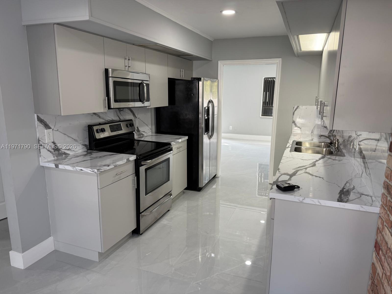 A modern kitchen features gray cabinets, marble-patterned countertops, stainless steel appliances, and light tile flooring — 2700 N 34th Ave # I, Hollywood FL 33021, HOLLYWOOD, FL