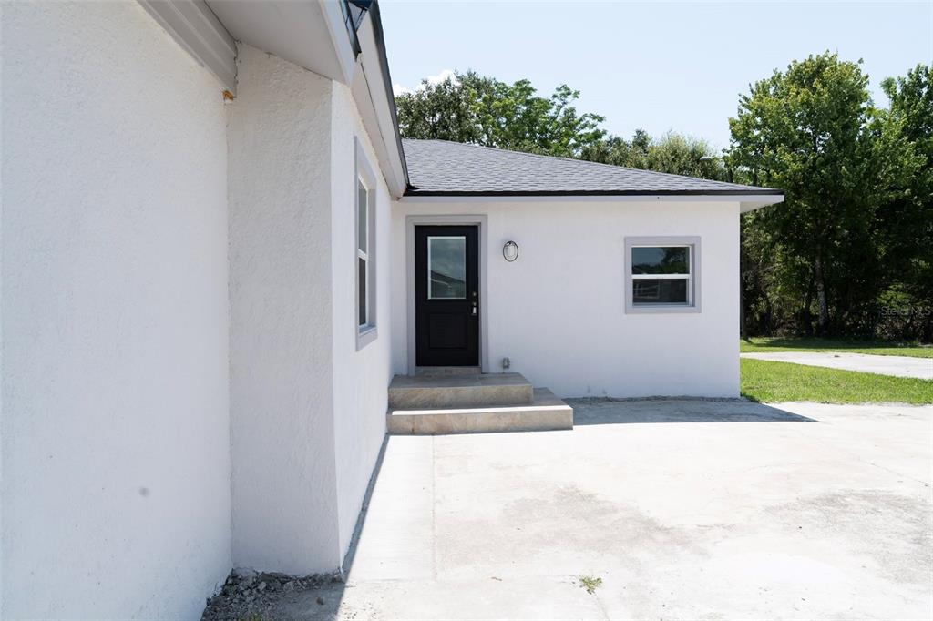 A white stucco house exterior features a black door, concrete steps, and a gray roof — 689 BETHUNE AVENUE, WINTER GARDEN, FL