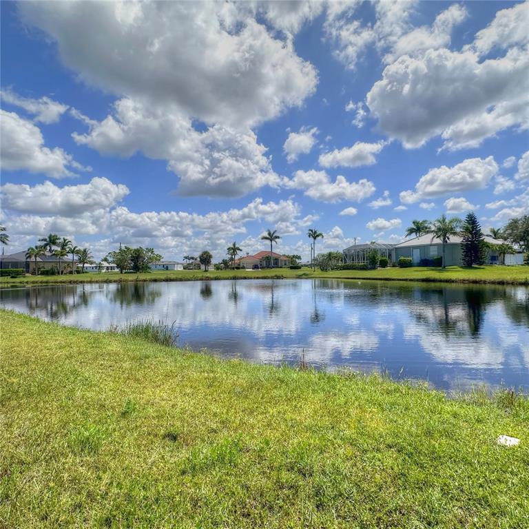 A grassy lawn overlooks a pond with houses and palm trees in the background — 17294 COMINGO LANE, PUNTA GORDA, FL
