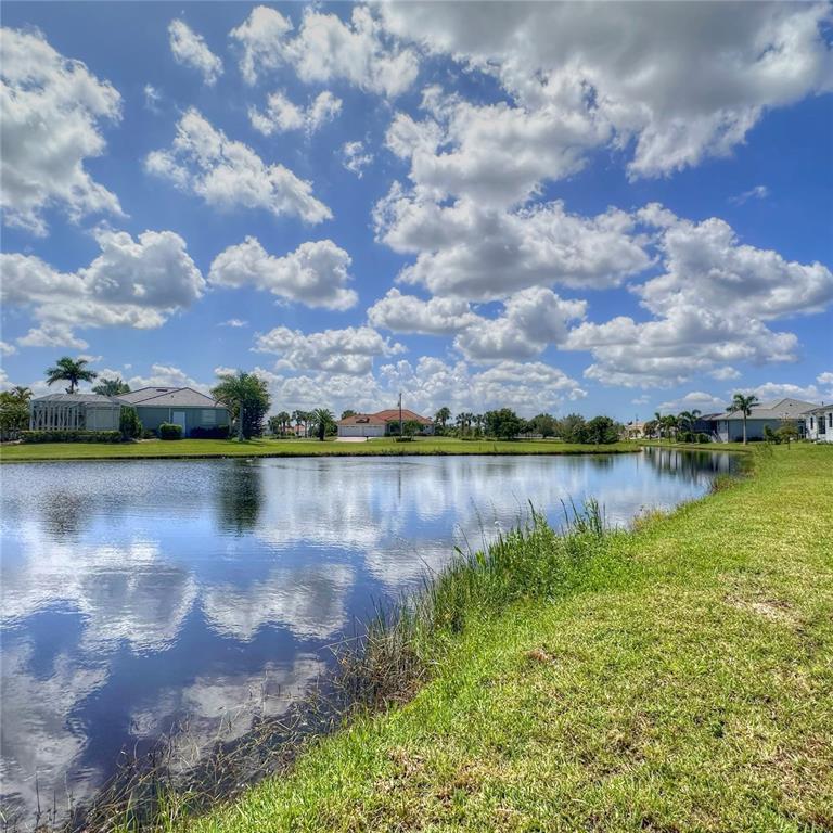 A view of a calm pond surrounded by grassy lawns and residential houses under clouds — 17294 COMINGO LANE, PUNTA GORDA, FL