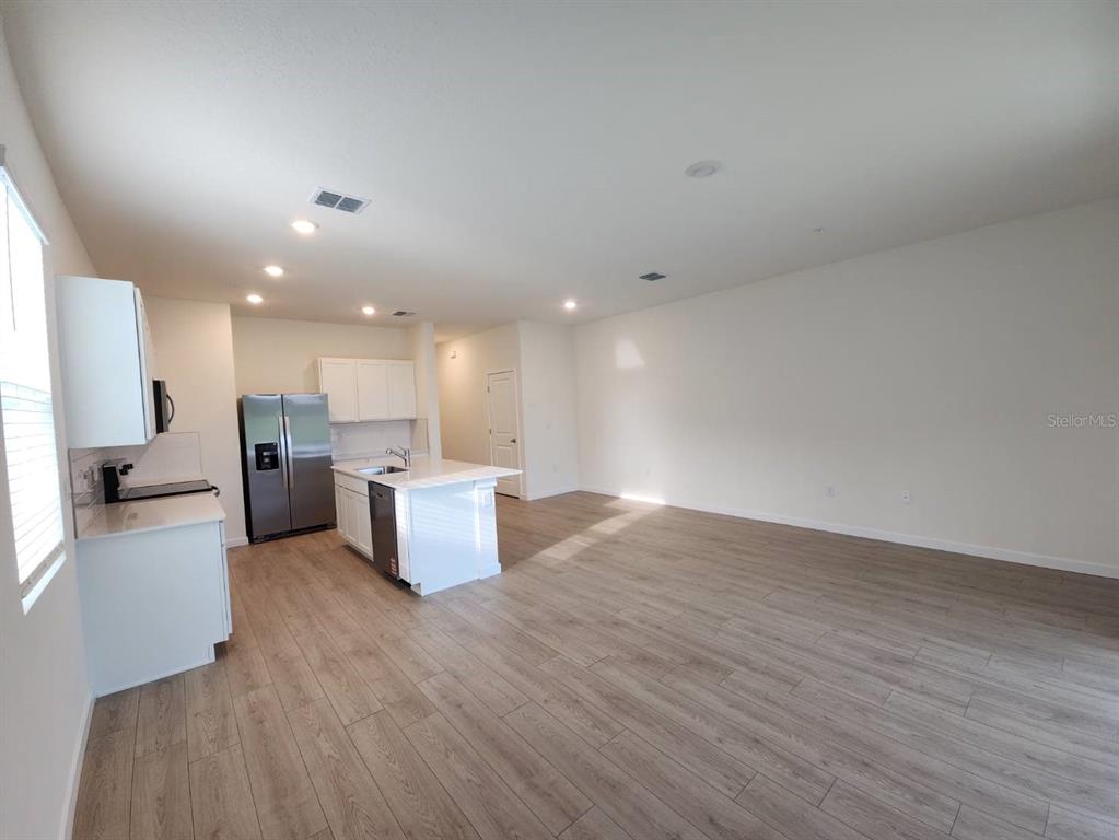 An open-concept kitchen and living area features white cabinets, stainless steel appliances, and wood-look flooring — 3371 CHROMA STREET, ORLANDO, FL