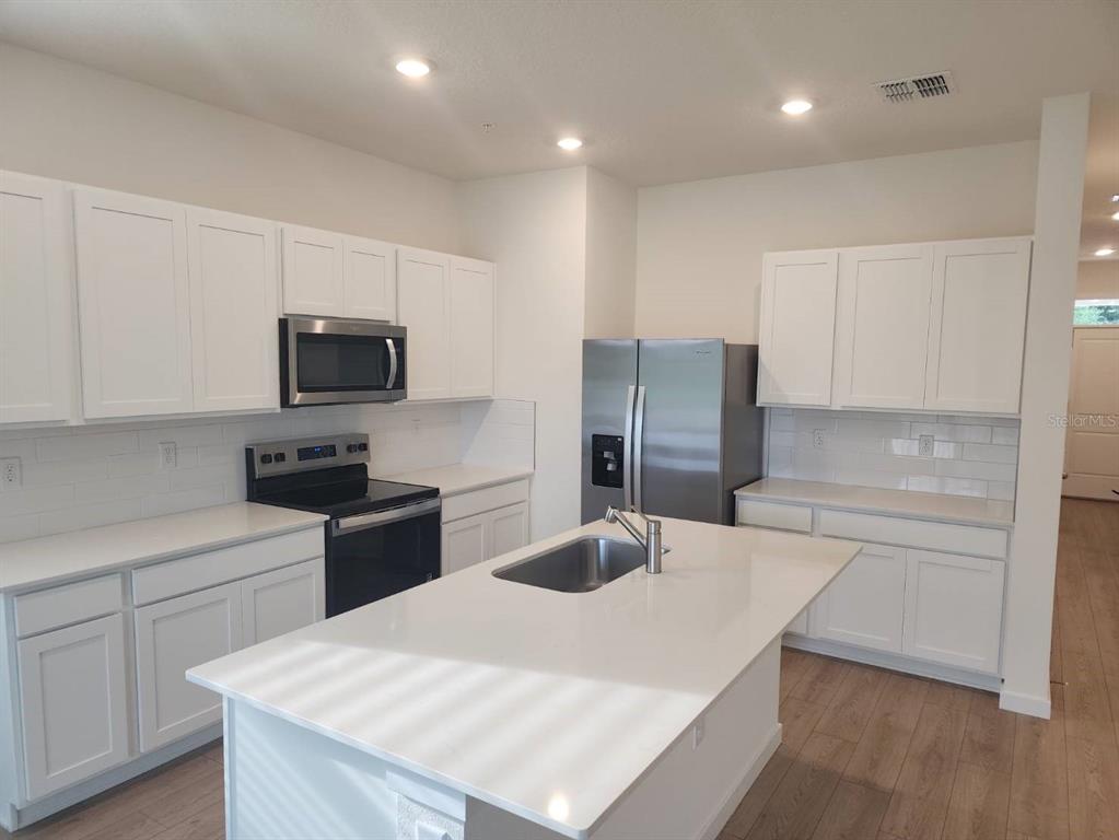 A modern kitchen features white cabinets, stainless steel appliances, a center island, and wood-look flooring — 3371 CHROMA STREET, ORLANDO, FL