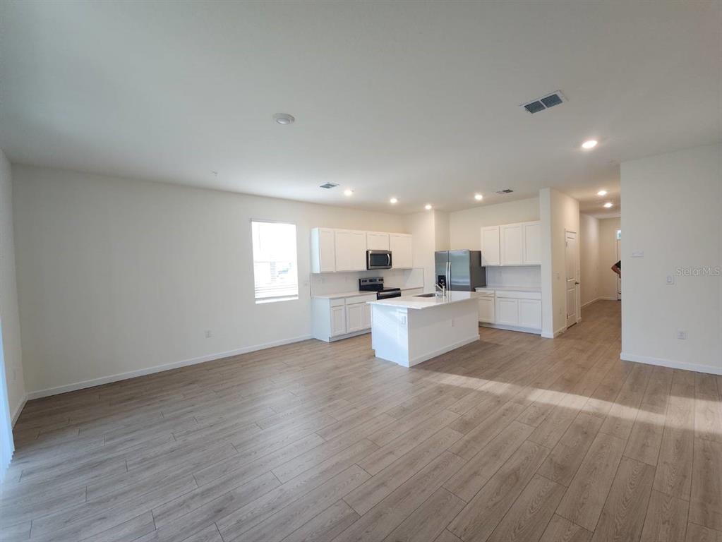 An open-concept kitchen with white cabinets and an island overlooks a spacious living area — 3371 CHROMA STREET, ORLANDO, FL