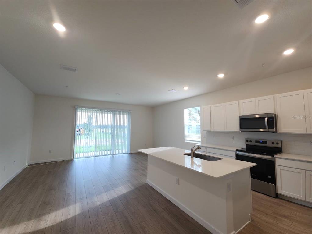 A kitchen with white cabinets and an island opens to a living area with sliding doors — 3371 CHROMA STREET, ORLANDO, FL