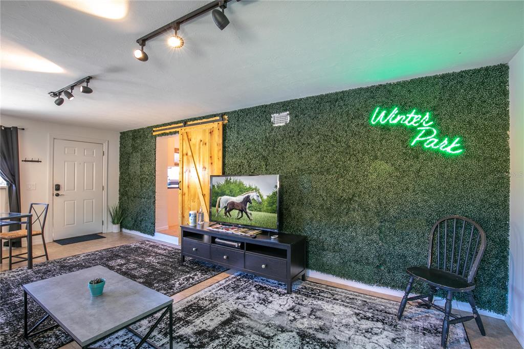 A living room features a green faux-foliage wall with a neon sign and barn door — 901 HARMON AVENUE, WINTER PARK, FL