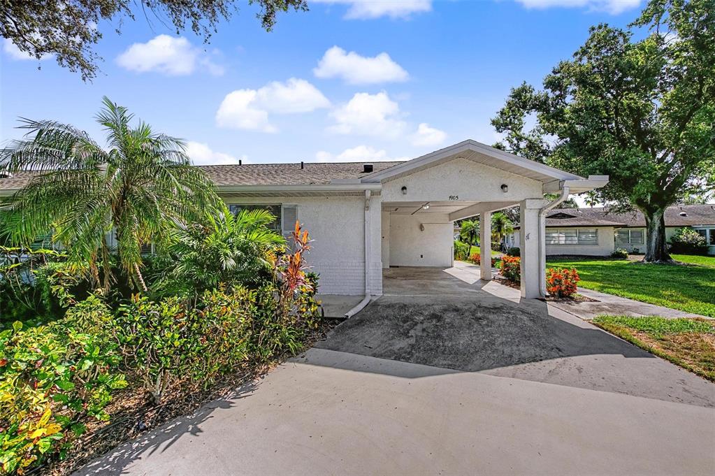 A single-story house with a white exterior, a covered carport, and surrounding tropical landscaping — 1905 HANSON COURT UNIT 305, SUN CITY CENTER, FL