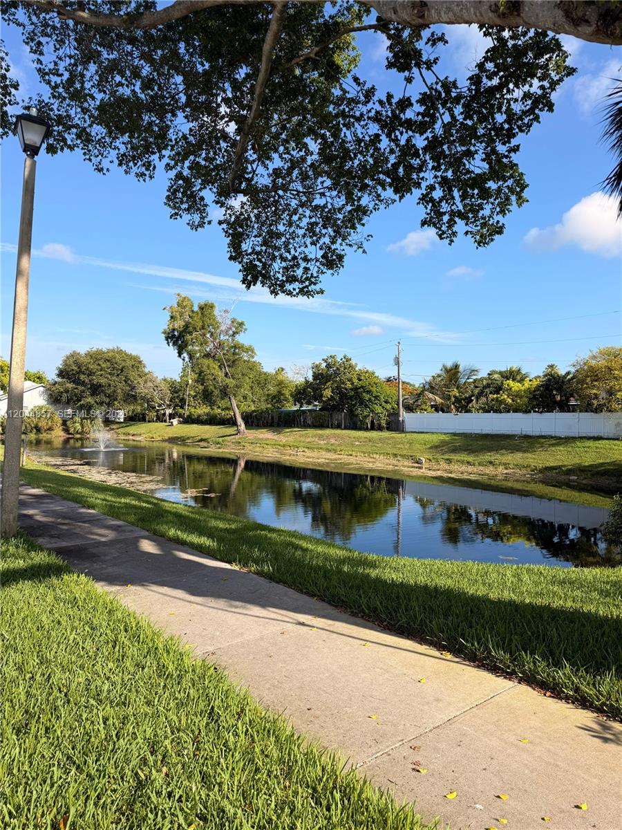 A paved sidewalk runs alongside a narrow pond with a fountain under a blue sky — 266 NW 60th Ave # 266, Margate FL 33063, MARGATE, FL