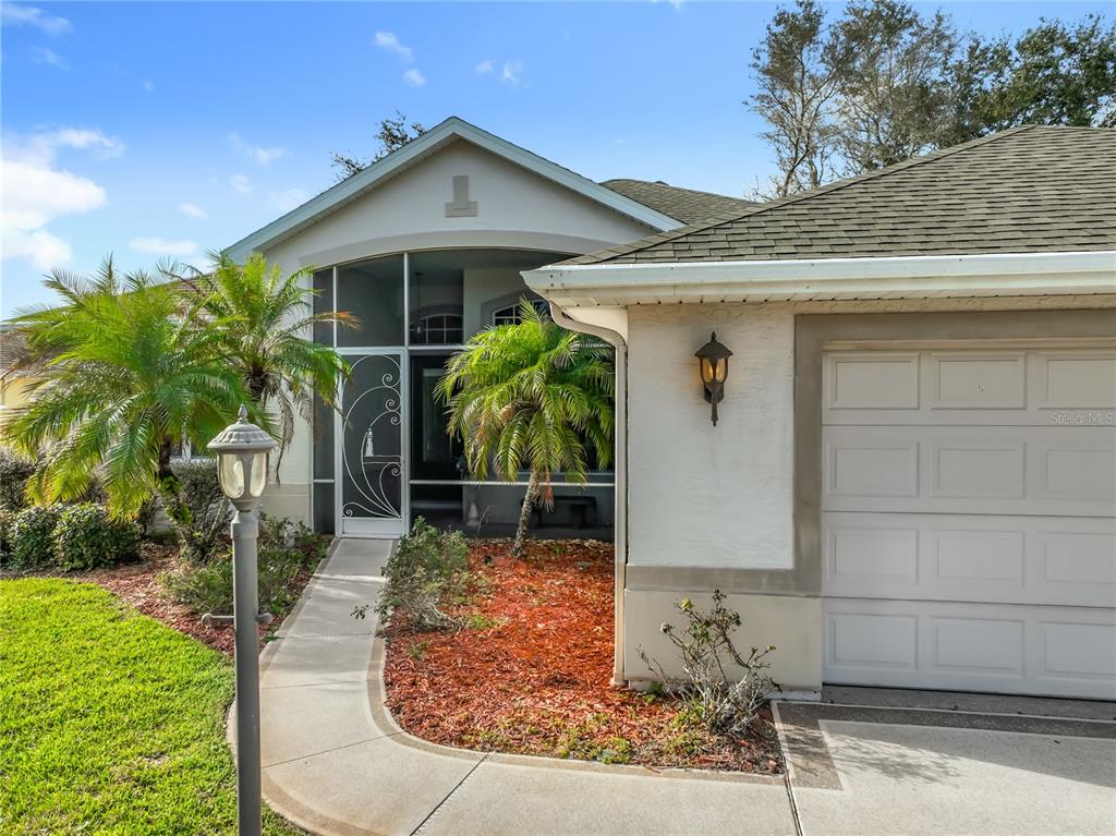 A house exterior features a screened entryway, a garage, a palm tree, and a walkway — 5685 GULF STREAM STREET, TAVARES, FL