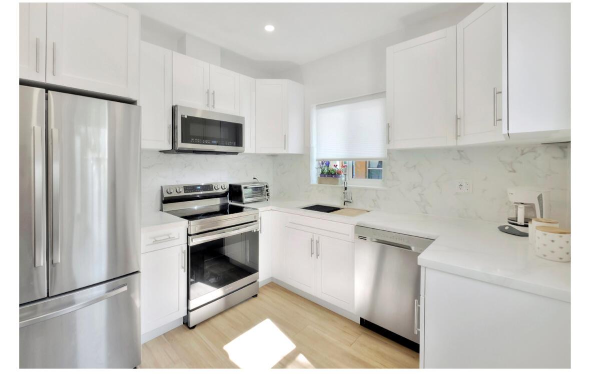 A modern kitchen features white cabinets, stainless steel appliances, and light wood flooring — 7825 Byron Avenue, Miami Beach FL 33141, MIAMI BEACH, FL