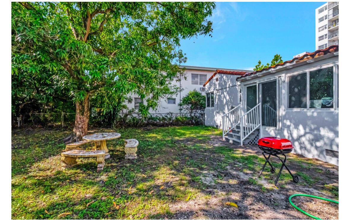 A backyard features a stone table and benches under a tree near a house exterior — 7825 Byron Avenue, Miami Beach FL 33141, MIAMI BEACH, FL