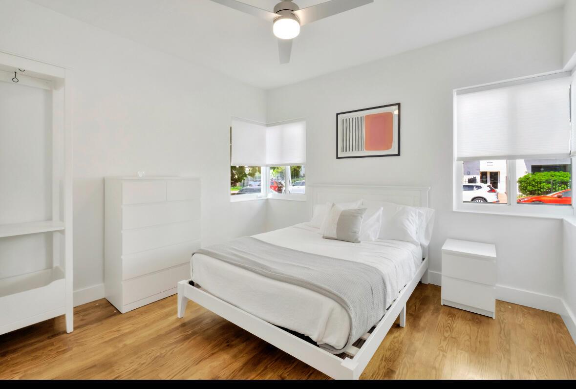 A bright bedroom features a white bed, dresser, shelving unit, and light wood flooring — 7825 Byron Avenue, Miami Beach FL 33141, MIAMI BEACH, FL