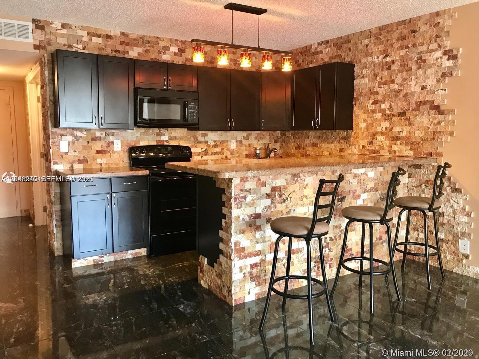A kitchen features dark cabinets, a stone-tiled backsplash, a breakfast bar, and dark tile flooring — 600 SE Three Islands Blvd # 1018, Hallandale Beach FL 33009, HALLANDALE BEACH, FL